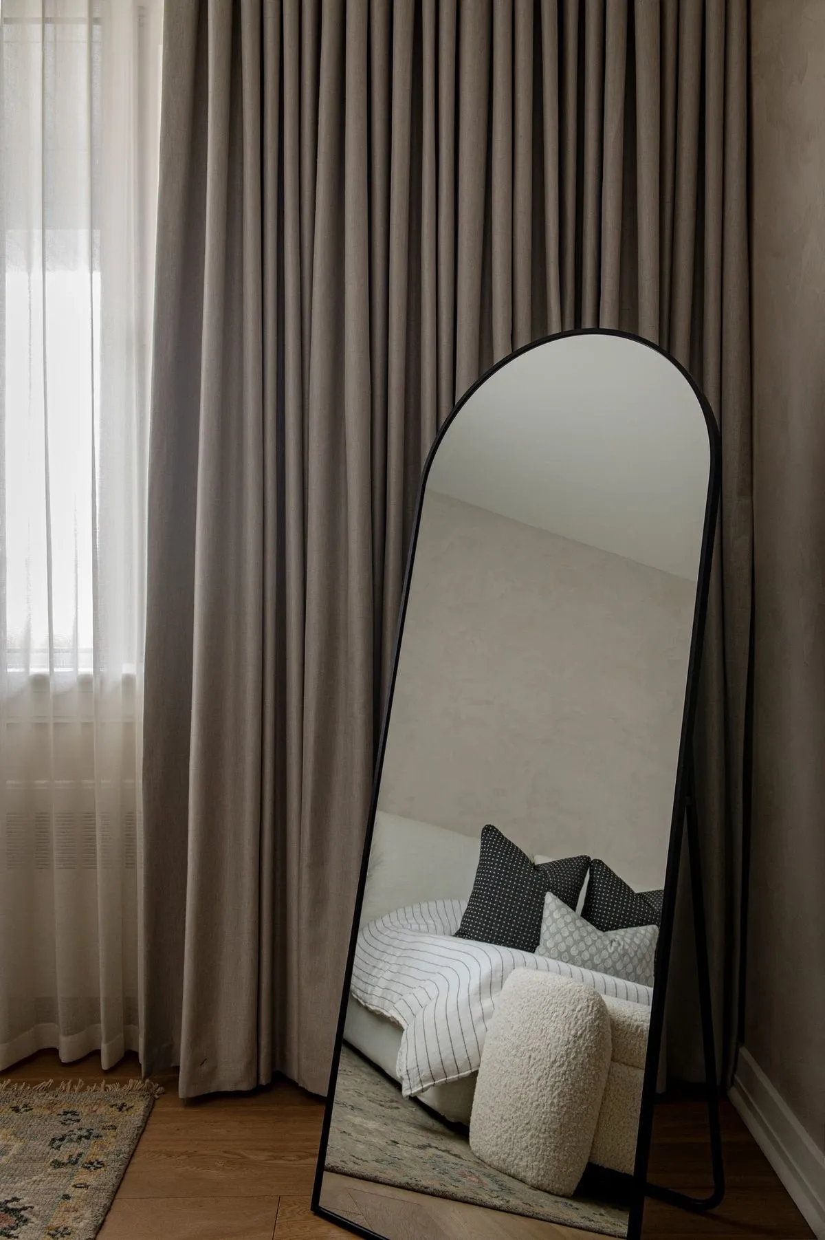 Espejo arqueado de cuerpo entero con marco negro de herrería instalado en habitación moderna